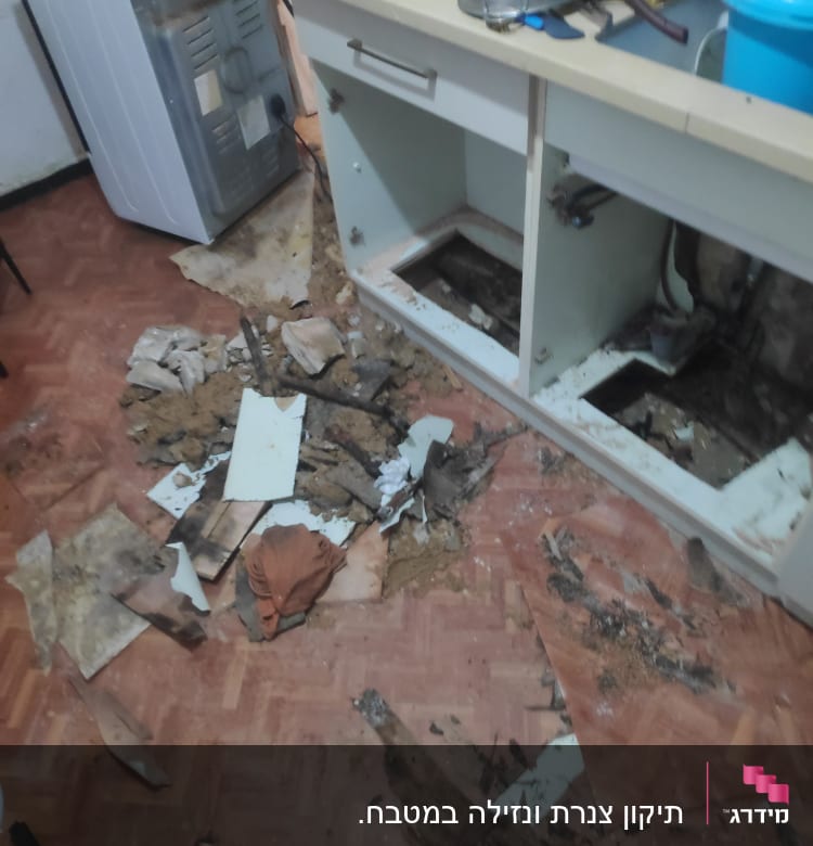 ארון מטבח פתוח עם צנרת חשופה ולכלוך על הרצפה